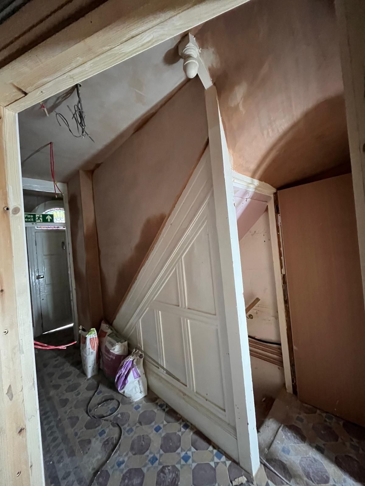 Pink skimmed walls under stairs with mosaic tile floor and stained glass beyond