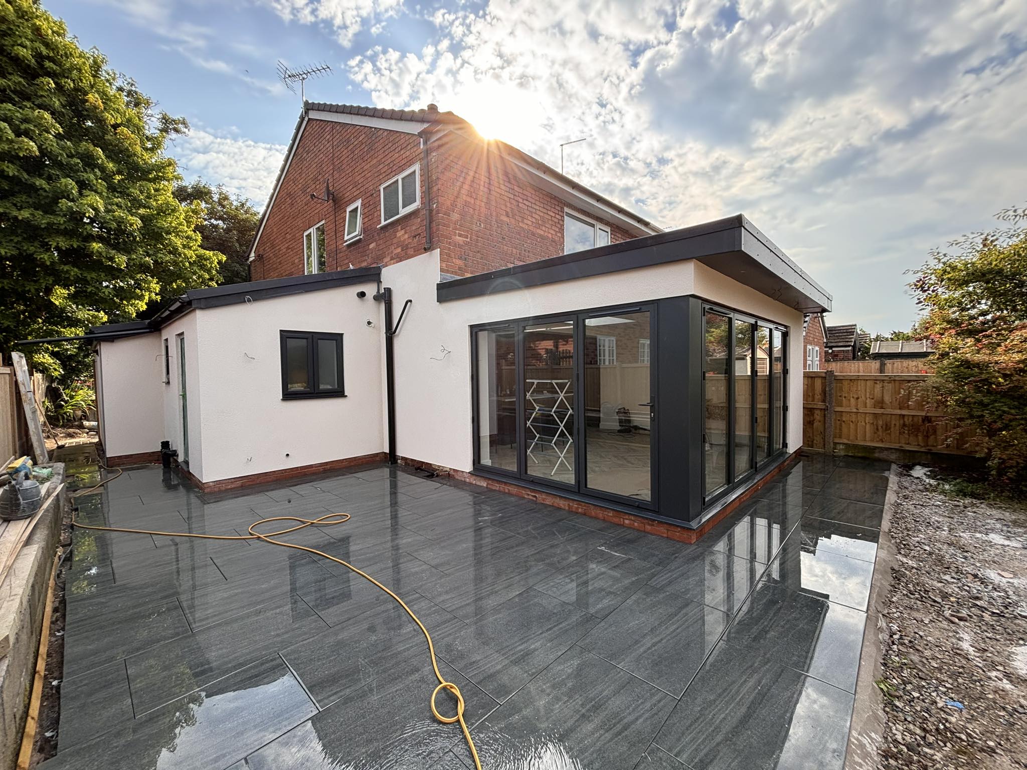 Modern white-rendered single-storey extension with black aluminium sliders and grey porcelain patio finished by JE Plastering